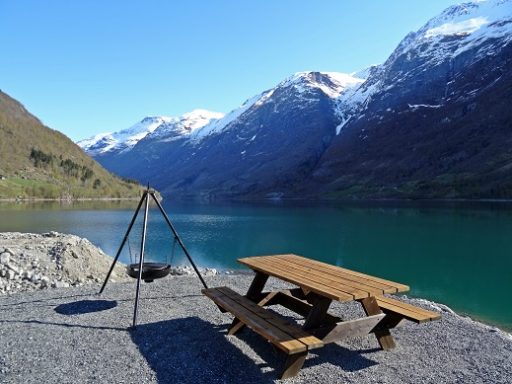 Une table de pique-nique au bord d'un lac, avec des montagnes enneigées en arrière-plan.