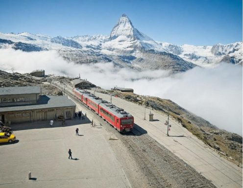Gare du Gornergrat Gare ferroviaire avec un train rouge, montagnes en arrière-plan, entourée de nuages et de neige.