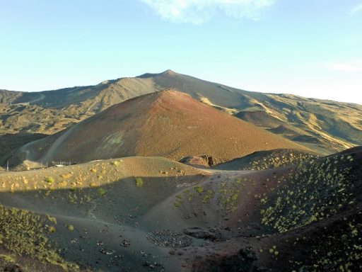 Vue d'un volcan (Etna) avec des pentes colorées, entouré de paysages montagneux.