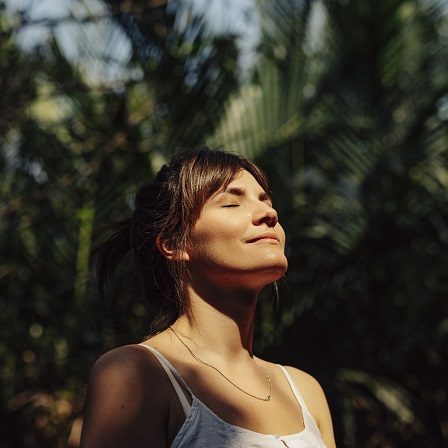 Femme souriante avec les yeux fermés, au milieu de la nature luxuriante.