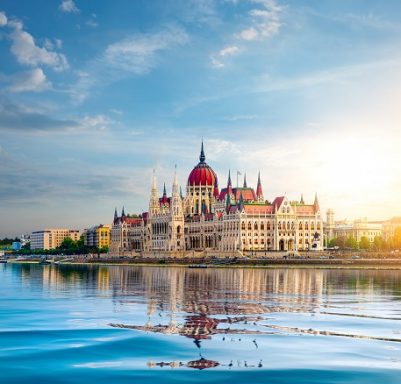 Parlement hongrois au bord du Danube à Budapest, avec un ciel bleu et des reflets sur l'eau.
