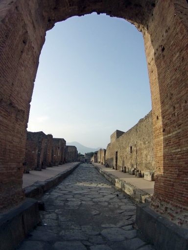 Ruines de Pompéi avec une voie pavée sous un arc en brique. Ciel clair en arrière-plan.
