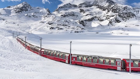 Train Bernina Express Train rouge serpentant à travers une étendue de neige avec des montagnes en arrière-plan.