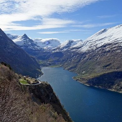 Vue panoramique du Geirangerfjord, en Norvège, entouré de montagnes enneigées et de vallées verdoyantes.