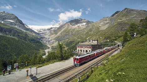 Train Bernina Express Gare ferroviaire dans un paysage montagneux, avec une végétation luxuriante et un ciel bleu.