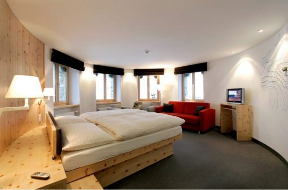 Kulmhotel Gornergrat Chambre moderne avec lit double, canapé rouge et fenêtres éclairant l'espace.
