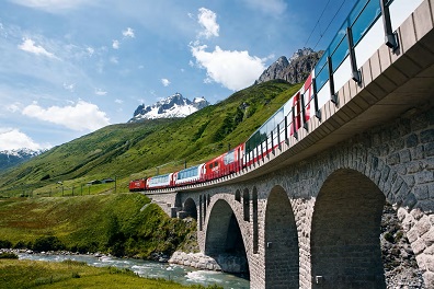 Glacier express Train rouge traversant un pont en pierre, entouré de montagnes verdoyantes.