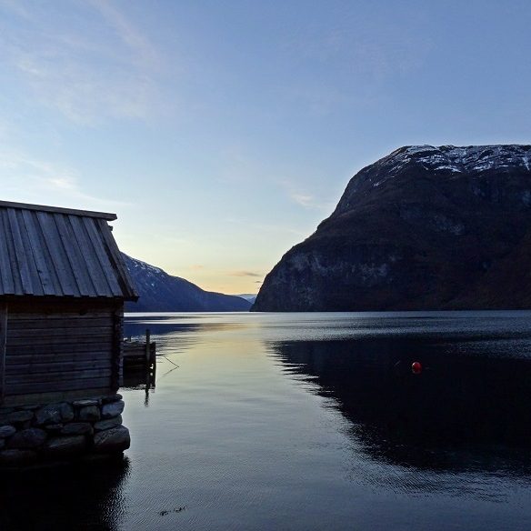 Reflet d'une montagne dans un fjord, avec une cabane en bois au premier plan.