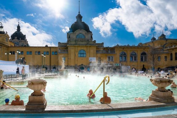 Bains thermaux Széchenyi avec bâtiment historique, vapeur d'eau et ciel dégagé.